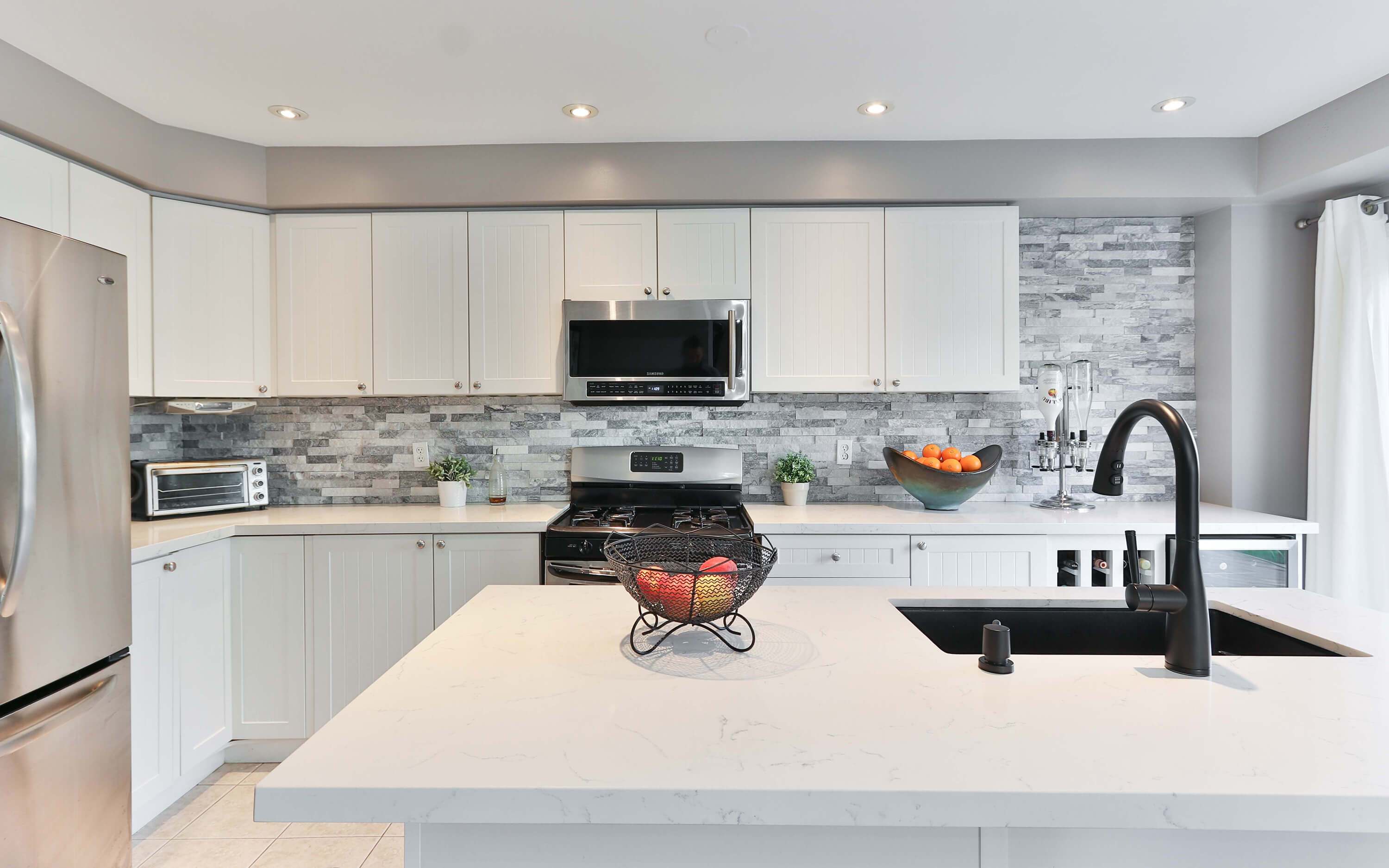Modern kitchen with white quartz benchtops, a black sink with black fittings and a grey tile backdrop